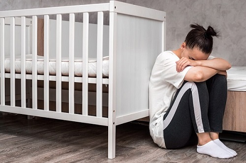 Kobieta cierpiąca na depresję poporodową siedzi przy łóżeczku dziecięcym