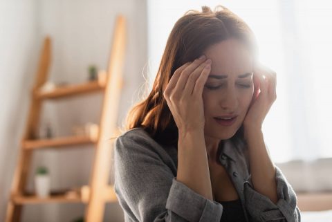 Kobieta cierpiąca na migrenę trzyma się za skronie
