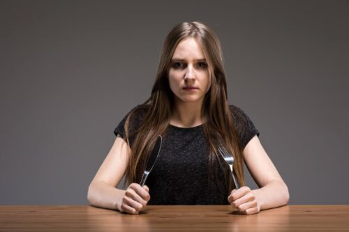 Kobieta z zespołem łaknienia spaczonego siedzi przy pustym talerzu